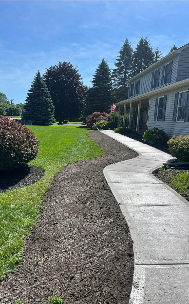 A new curved concrete walk up to a front porch, with a band of fresh topsoil along the lawn beside it