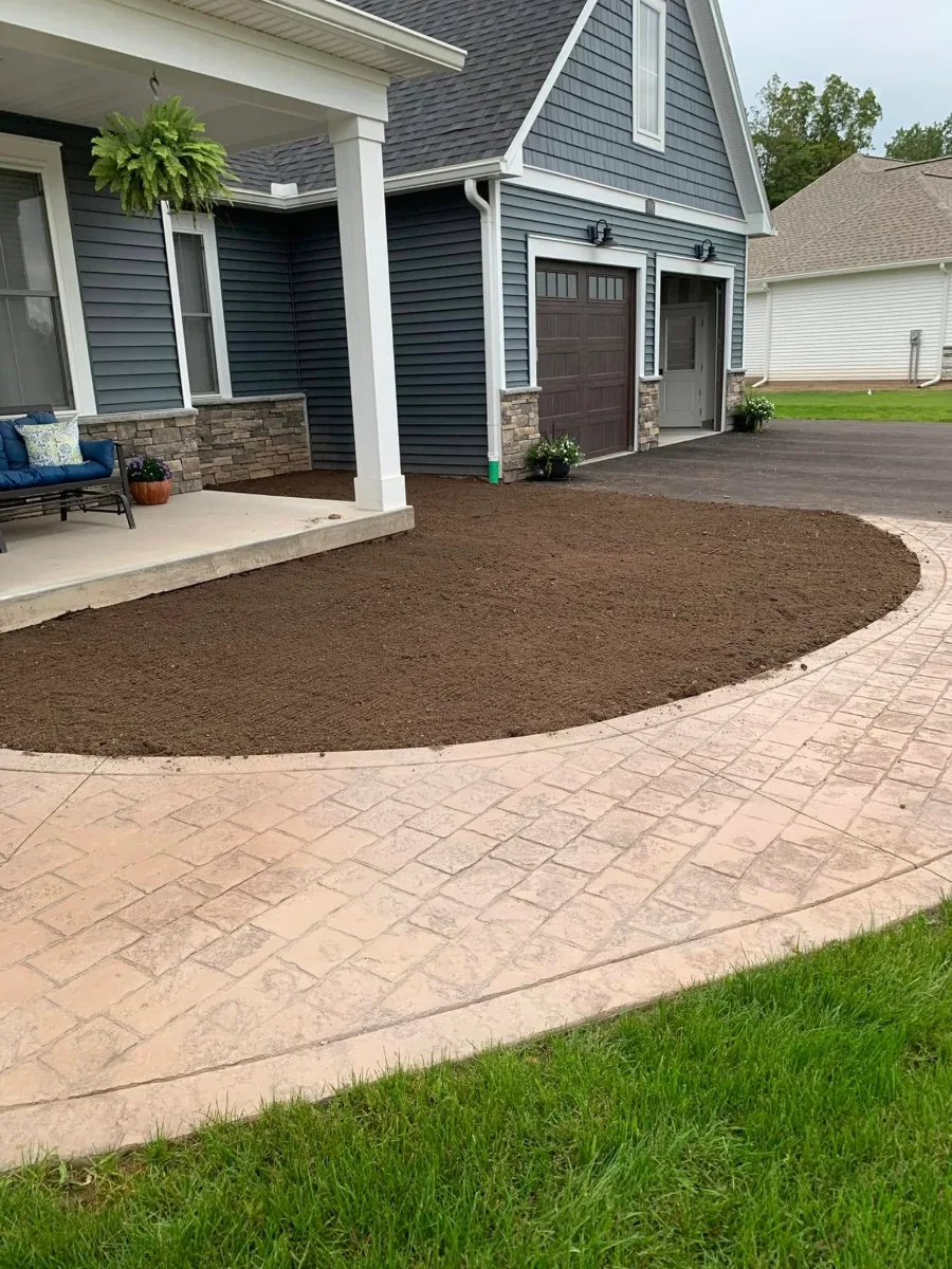 A new stamped concrete walk curving past a front porch, with the ground beside it topsoiled for seed